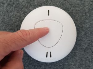 finger pressing photoelectric smoke alarm to test it