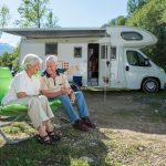 Grey nomad couple sitting outside campervan