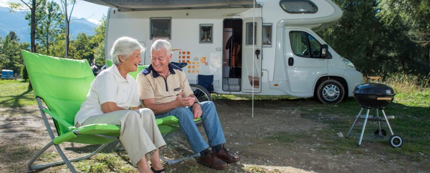 Grey nomad couple sitting outside campervan